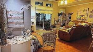 A cozy living room with a sofa, chairs, and a fireplace. There is a large window with curtains, a ceiling fan, and a wall with decorative items. - Peaceful 3-bedroom house with AC in Flagler Beach (Flagler Beach)