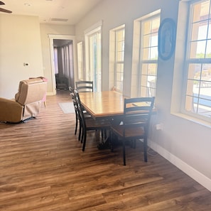 A dining area with a wooden table and chairs, a massage chair, and large windows.
