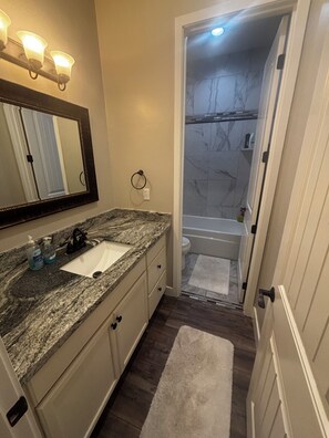 A bathroom with a granite countertop, a sink, a mirror, a towel ring, and a shower with marble tiles.