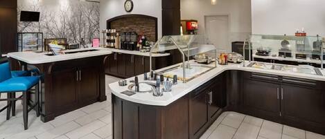 A modern kitchen with a central island, bar stools, and a built-in refrigerator.