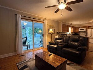 A living room with a leather sofa, a wooden coffee table, a ceiling fan, and a sliding glass door leading to a balcony.