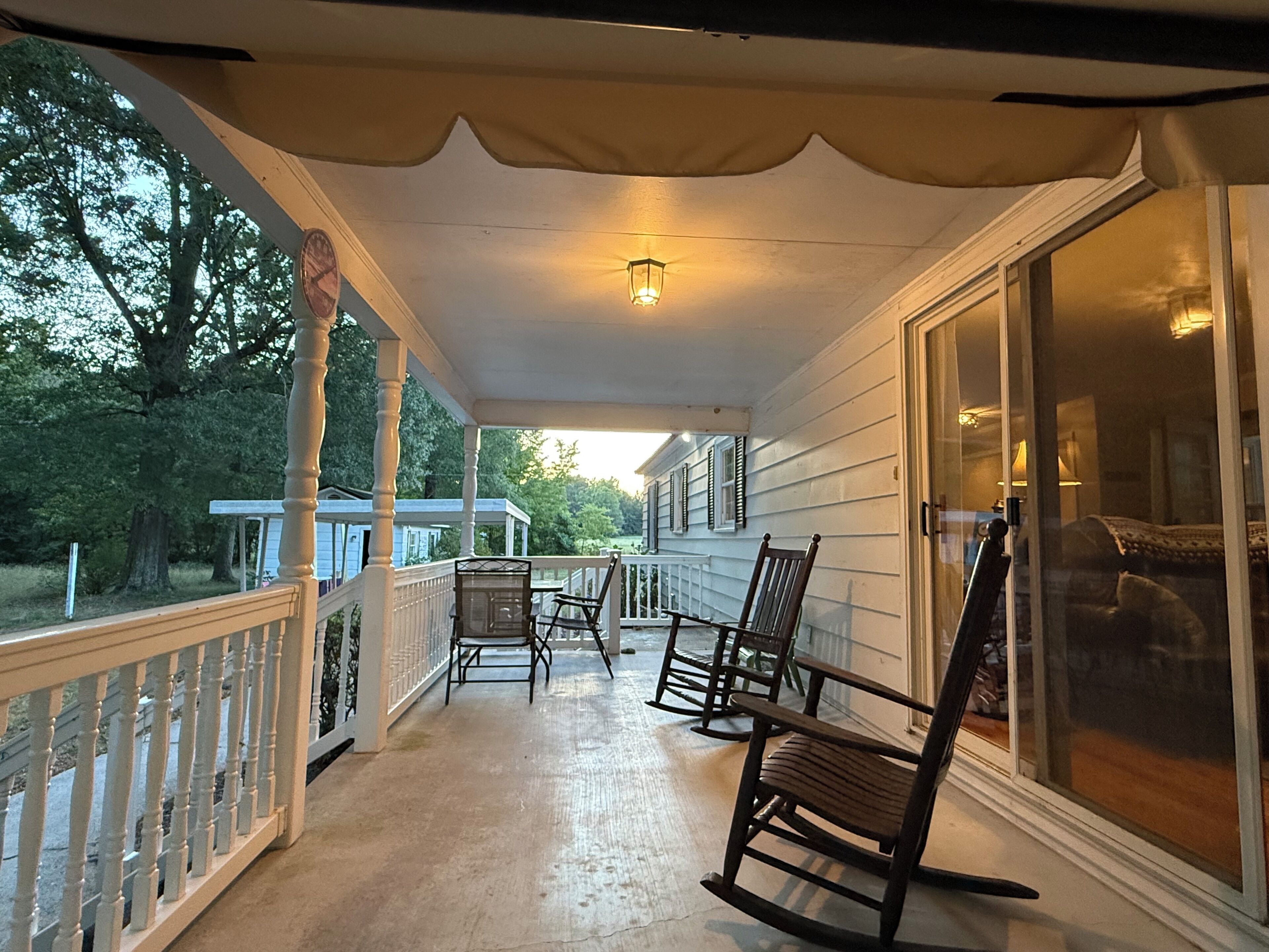 Une véranda couverte avec une balustrade, une table et deux fauteuils à bascule.
