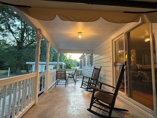 A covered porch with a railing, a table, and two rocking chairs.
