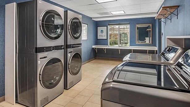 Une buanderie équipée de machines à laver et de sèche-linge superposés, d’un banc et d’une fenêtre donnant sur un paysage agréable.