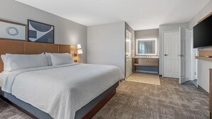 A hotel room with a large bed, a desk, a TV, and a bathroom visible through an open door. - Rocklin King Suite | Pool + Free Daily Breakfast (Rocklin)
