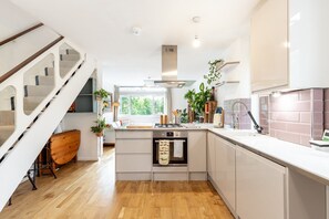 A modern kitchen with a central island, wooden flooring, and a staircase with a mirrored wall. - Stylish Clapham Retreat Near the Common (London)