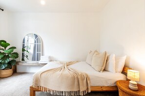A bedroom with a bed, a bedside lamp, a window with a view, and a potted plant. - Stylish Clapham Retreat Near the Common (London)