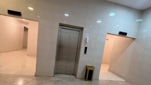 Um hall amplo com piso de mármore, um elevador e uma lixeira.