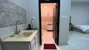 Cozinha moderna com pia, chaleira e fogão, adjacente a um banheiro com vaso sanitário e chuveiro.