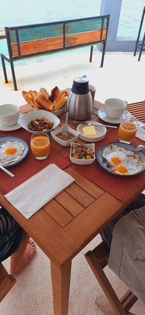 A breakfast table with various food items, a coffee pot, and a view of the sea. - Manihi miki lodge (Manihi)
