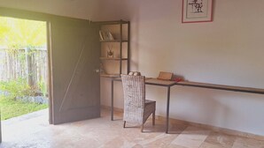 A room with a desk, chair, bookshelf, and a door leading to a garden.