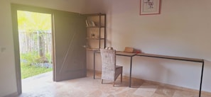 Una habitación con escritorio, silla, estantería y puerta que da a un jardín.