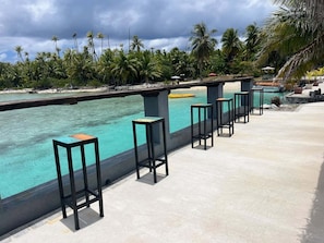 Zona junto a la piscina con un suelo de hormigón, una fila de taburetes negros y vista a una piscina turquesa.