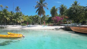 A beach with clear turquoise water, yellow kayaks, and a boat docked near the shore.
