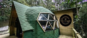 A hexagonal-shaped building with a green roof, a wooden deck, and a black circular sign with the name 'Sanaya' and the number '360'. - Glamping Cabin in a Private Forest, 15 Minutes from José María Córdova Airport (Rionegro)