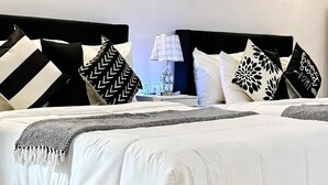 A modern bedroom with a black and white color scheme, featuring a large bed with multiple pillows, a bedside table with a lamp, and a wall clock.