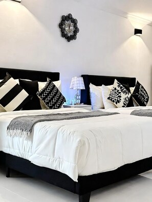 A modern bedroom with a black and white color scheme, featuring a large bed with multiple pillows, a bedside table with a lamp, and a wall clock. - Garden Ocean View Oasis at the West Signature (Negril)