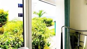 A room with a view of a lush garden and a building across the street.