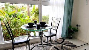 A small dining area with a glass table and black chairs, a potted plant, and a view of greenery outside.