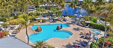 A resort with a central swimming pool, sun loungers, palm trees, and a view of the ocean.