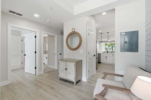 A modern interior with a hallway leading to a kitchen, a wooden cabinet, and a round mirror on the wall. - 314 - Renovated First Floor with Golf Views (Naples)
