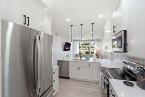 A modern kitchen with stainless steel appliances, white cabinetry, and pendant lighting. - 314 - Renovated First Floor with Golf Views (Naples)