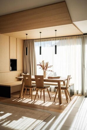 A modern dining area with a wooden table, chairs, pendant lights, and a view through sheer curtains. - Lebe' Oetz im Ötztal  (Oetz)