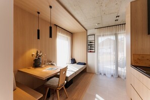 A compact living space with a wooden dining table, a bench, a bed, and a kitchenette. - Lebe' Oetz im Ötztal  (Oetz)