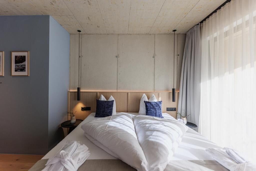 Une chambre d’hôtel avec un lit, des tables de chevet, une petite table et une fenêtre avec des rideaux.