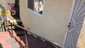 Eine Treppe führt zu einem Gebäudeeingang, ausgestattet mit einem Metallgeländer, einer Tür mit dekorativem Gitter und einem Fenster mit Blick auf die Straße.