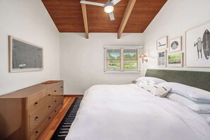 Ein Schlafzimmer mit einem Bett, einer Kommode, einem Deckenventilator, einem Fenster mit Jalousien und gerahmten Bildern an den Wänden.