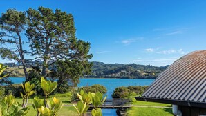 A lakeside view with a wooden building, a bridge over water, and surrounding greenery. - Ocean Breeze Family Haven - Pauanui Holiday Home (Pauanui)