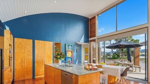 A modern kitchen with wooden cabinets, a built-in dishwasher, and a large island with a sink. - Ocean Breeze Family Haven - Pauanui Holiday Home (Pauanui)