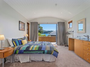 Ein Schlafzimmer mit Bett, Nachttisch, Lampe, Kommode und Blick ins Freie.