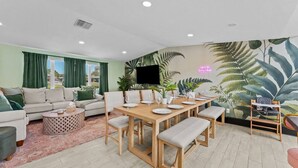 Ein Wohnzimmer mit einer Couch, einem Esstisch für vier Personen und einem an der Wand befestigten Fernseher.