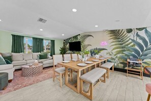A living room with a sofa, a dining table set for four, and a TV mounted on the wall. - Heated Pool~Spa~Mini Golf~Fire Pit~Game Room (Clearwater)