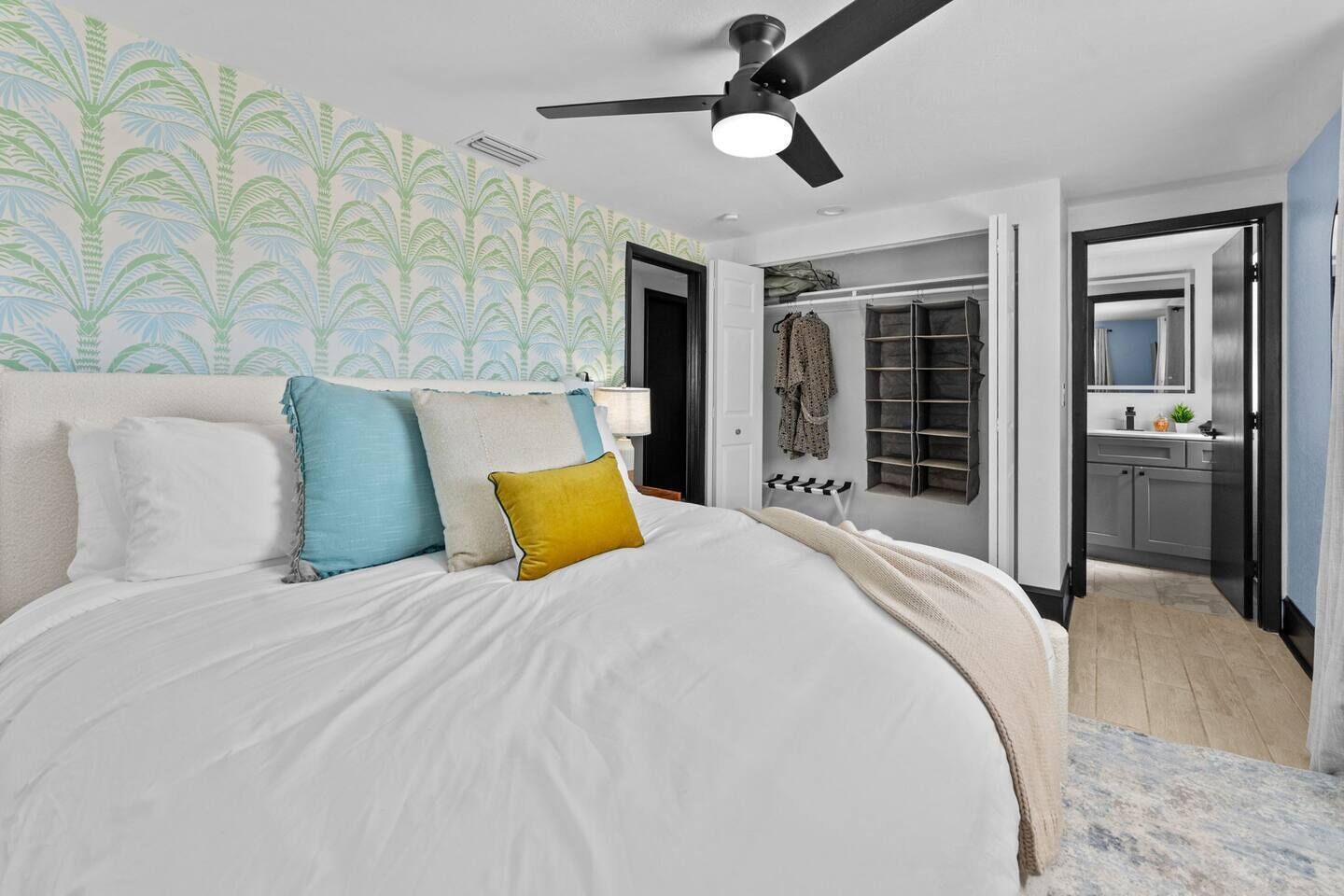 A bedroom with a bed, pillows, a ceiling fan, a walk-in closet, and a bathroom with a mirror.