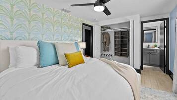 A bedroom with a bed, pillows, a ceiling fan, a walk-in closet, and a bathroom with a mirror.