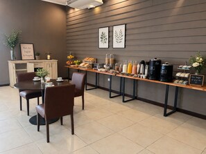 En morgenmadsbuffet med forskellige spiser og drikkevarer, en kaffestation og et skilt med en besked.
