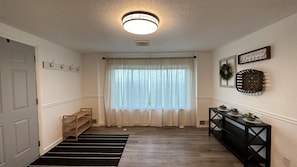 A hallway with a ceiling light, a window with sheer curtains, a coat rack, a bench, and a console table with plants. - Quiet Country Retreat East of Nappanee — Relax, Recharge, and Unwind (Nappanee)