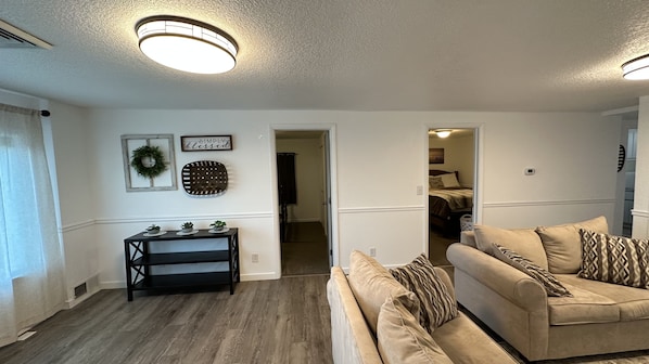 A living room with a sofa, a console table with plants, a ceiling light, and a doorway leading to a bedroom. - Quiet Country Retreat East of Nappanee — Relax, Recharge, and Unwind (Nappanee)