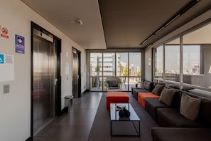 Eine moderne Hotelhalle mit Aufzug, Sitzgelegenheiten und großen Fenstern mit Blick auf die Stadt.