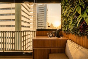 Un balcó amb vista a edificis alts, un taulell de fusta amb una cafetera i una paret coberta de plantes.