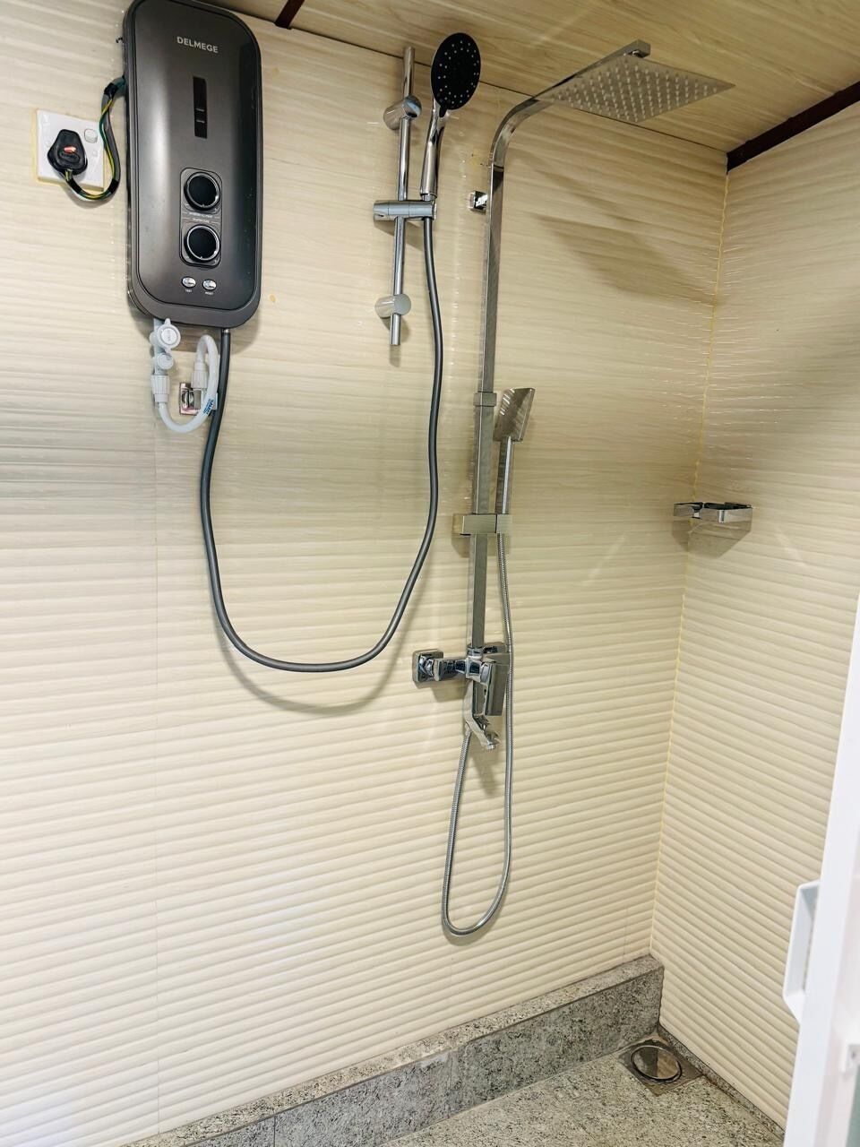 A shower with a handheld showerhead, a wall-mounted faucet, and a control panel.