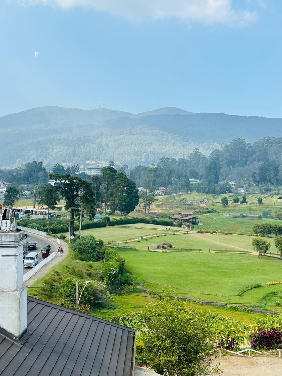 Vista de un paisaje verde con una carretera, edificios y colinas al fondo.