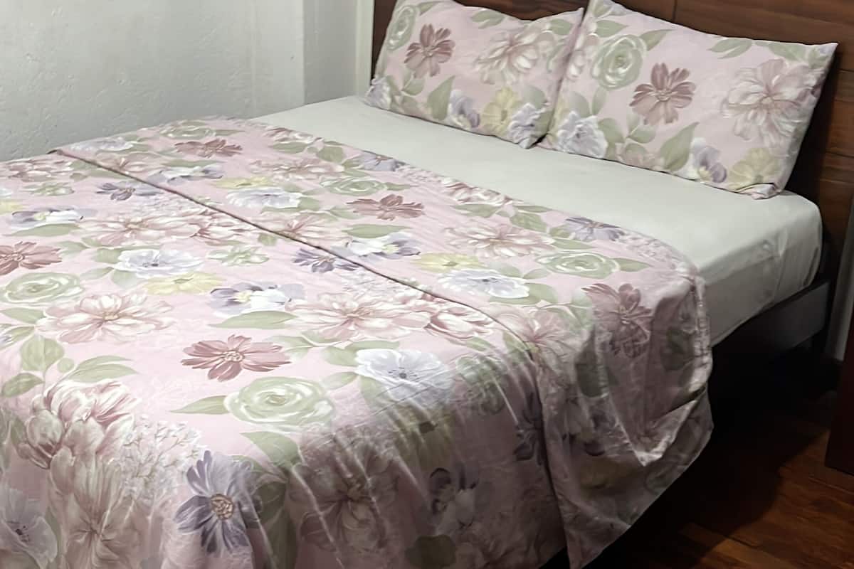 A bed with a floral bedspread, a wooden headboard, and a wooden floor.