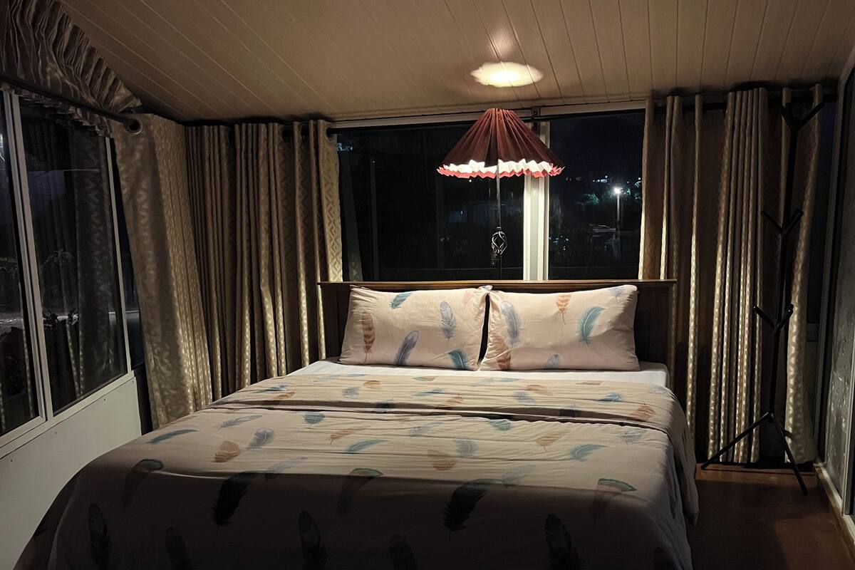 A bedroom with a bed, curtains, a window, and a ceiling light.