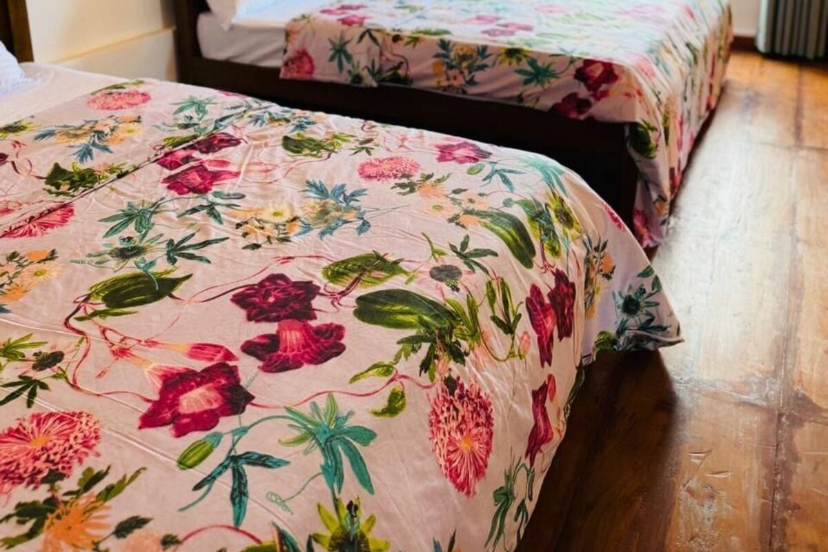 A room with two beds, floral bedspreads, a painting on the wall, and a window with curtains.