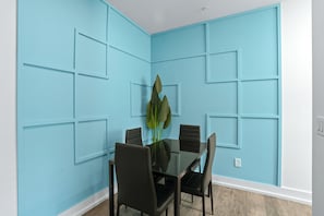 A dining area with a glass table surrounded by chairs, a plant in the center, and blue paneled walls. - Hyde Park 1/1 private residence 3 (Tampa)