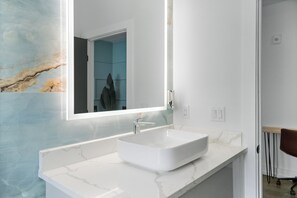 Ein modernes Badezimmer mit einem großen Spiegel, einer weißen Marmorplatte und einem eleganten weißen Waschbecken.